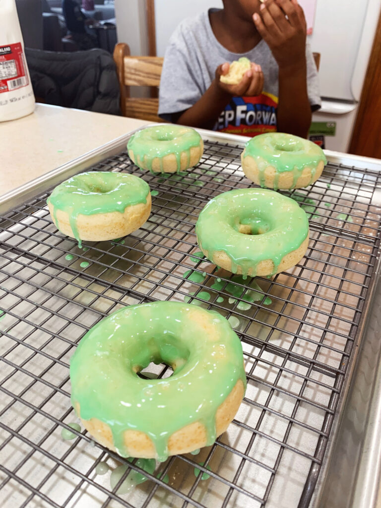 Five green glazed donuts on a cooling rack on a silver baking sheet