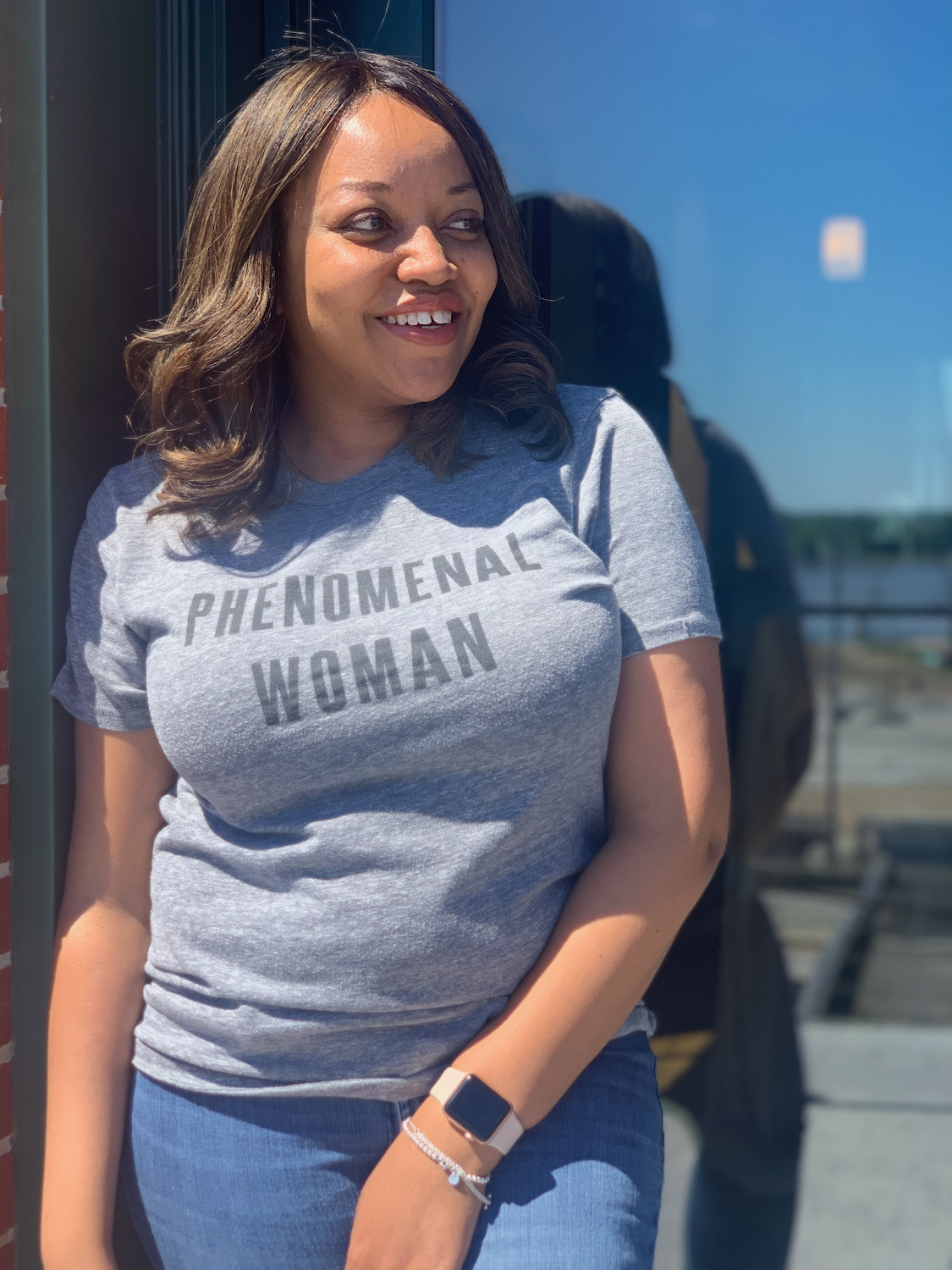 Smiling KB looking away on a sunny day. Wearing a gray t-shirt that says Phenomenal Woman