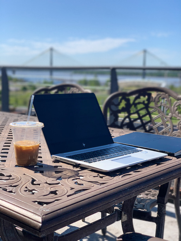 Laptop and iced coffee on outdoor deck overlooking river and bridge. Cracker Factory lodging during visit to Alton, Illinois