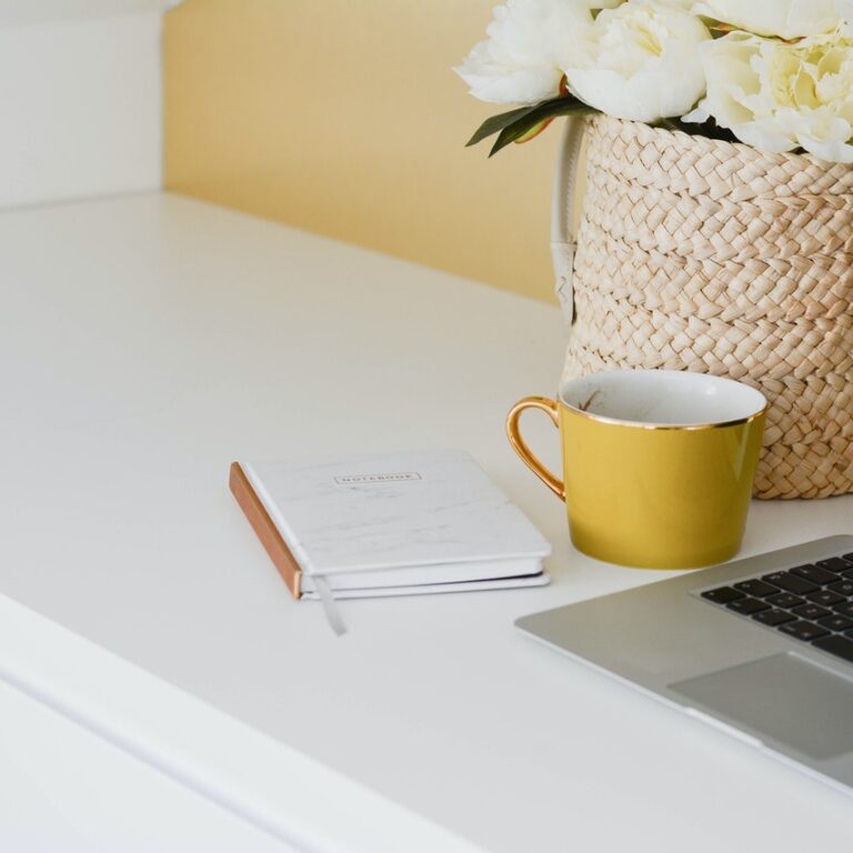 laptop on white counter with yellow coffee cup and notepad