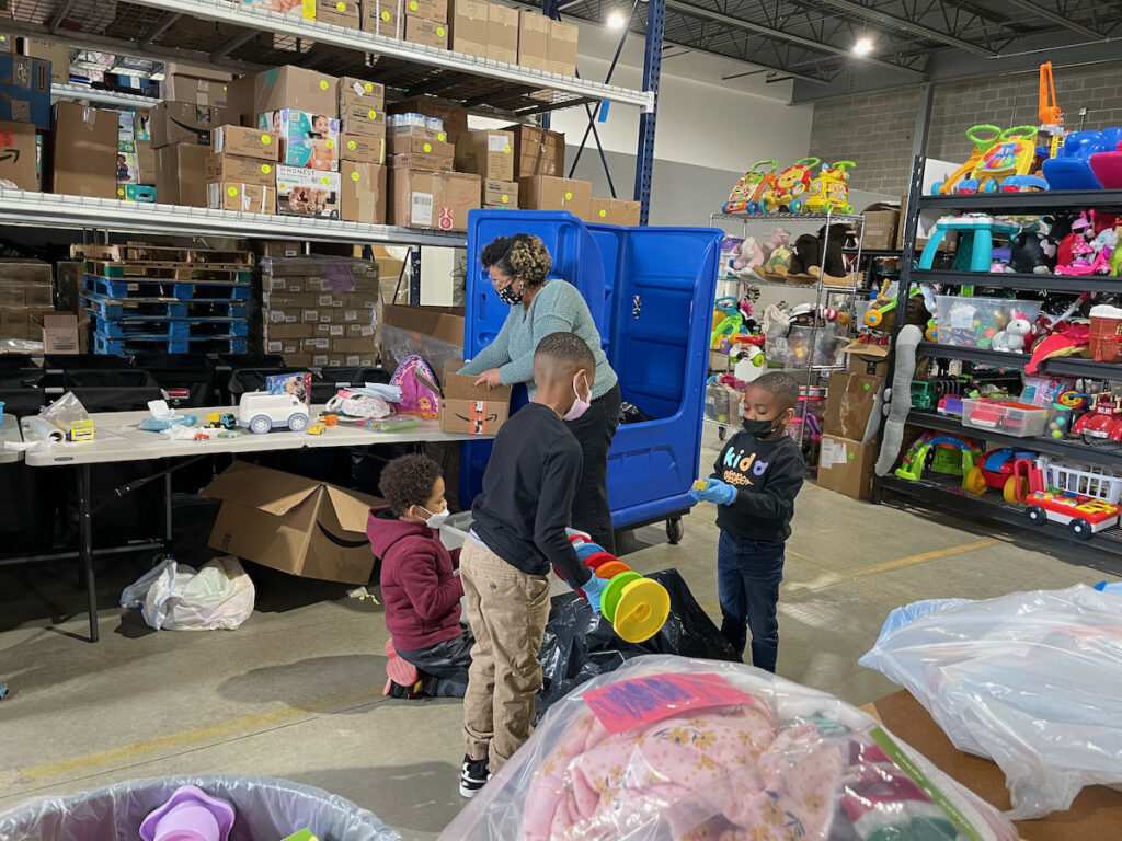 family volunteering in chicago with two boys. they are in a warehouse with tall shelves of boxes and toys in the background